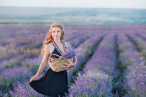 Mladá matka s mladou dcerou, usmívající se na poli levandule. Sedět na rukou matka a dcera. Dívka v barevné šaty a matka v tmavě modrých šatech. — Stock fotografie