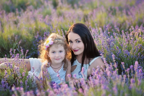 Young beautiful lady mother with lovely daughter walking on the lavender field on a weekend day in wonderful dresses and hats. — Stock Photo, Image
