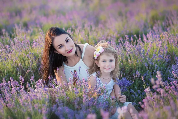 Молода красива леді мати з прекрасною дочкою, що йде на лавандовому полі у вихідний день у чудових сукнях та капелюхах . — стокове фото