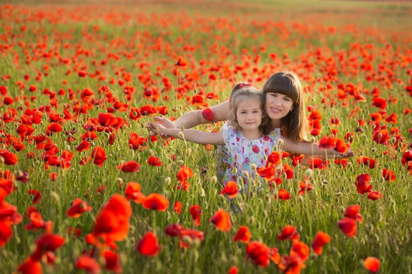 Madre e hija sonriendo en un campo de amapola. El Picnic en el campo de amapola. Caminar con la familia en el campo de amapola. Las amapolas del carro —  Fotos de Stock