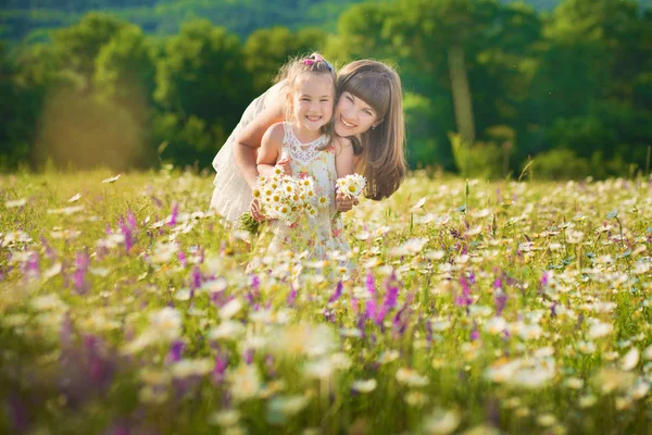 Mamma och dotter på picknick i fältet kamomill. Två vackra blondiner i kamomill fält på en bakgrund av häst. Mor och dotter omfamnar i fältet kamomill — Stockfoto