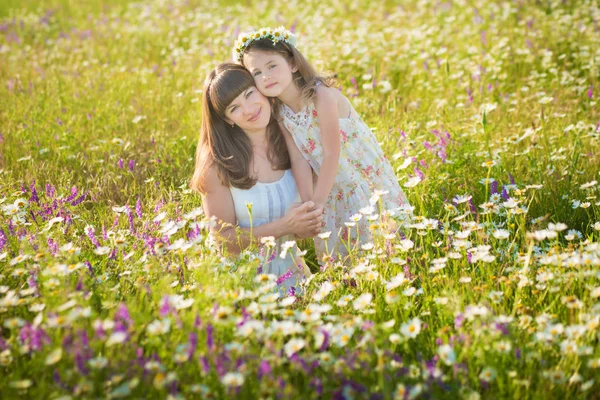 Mamma och dotter på picknick i fältet kamomill. Två vackra blondiner i kamomill fält på en bakgrund av häst. Mor och dotter omfamnar i fältet kamomill — Stockfoto