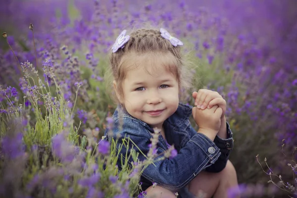 Pretty young girl sitting in lavender field in nice hat boater with purple flower on it. — Stock Photo, Image