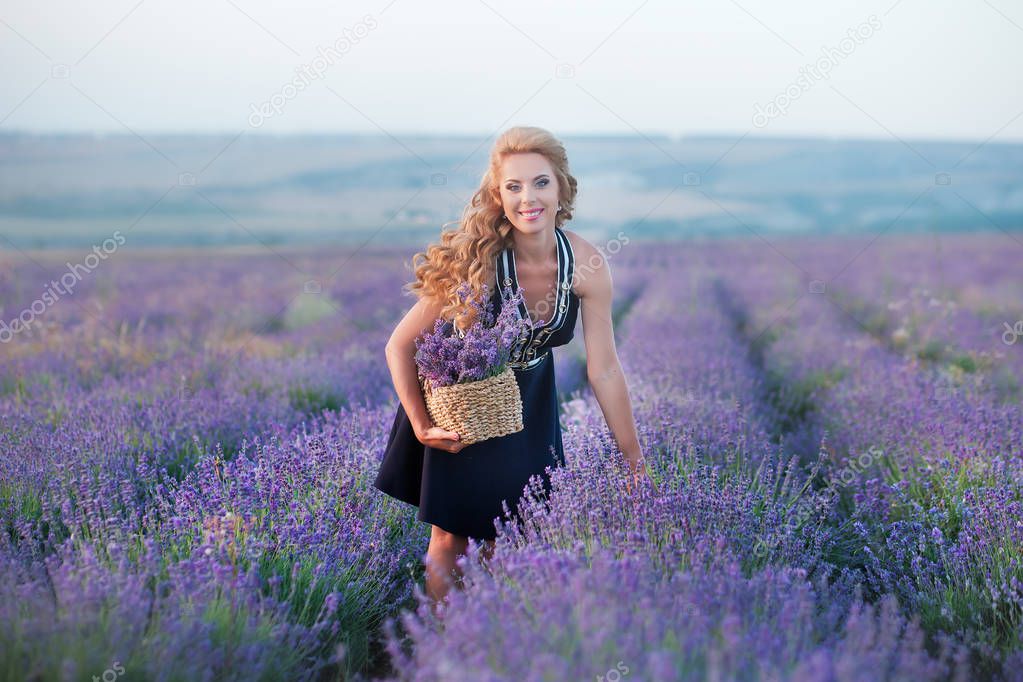 Young mother with young daughter smiling on the field of lavender .Daughter sitting on mother hands.Girl in colorful dress and mother in dark blue dress.