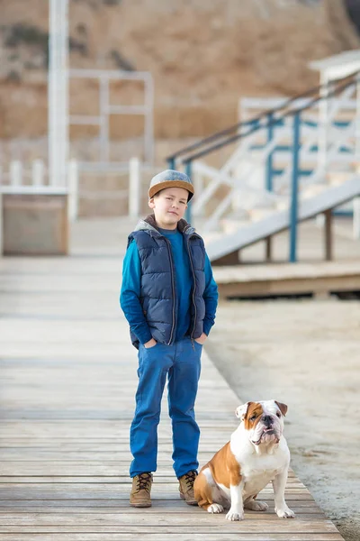Trevlig ser stilig pojke på stranden med bulldog — Stockfoto