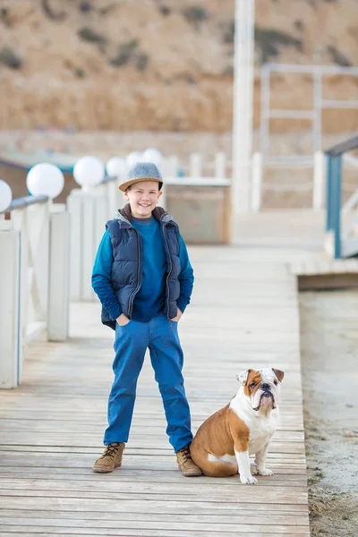 Trevlig ser stilig pojke på stranden med bulldog — Stockfoto