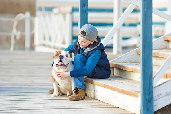 Trevlig ser stilig pojke på stranden med bulldog — Stockfoto