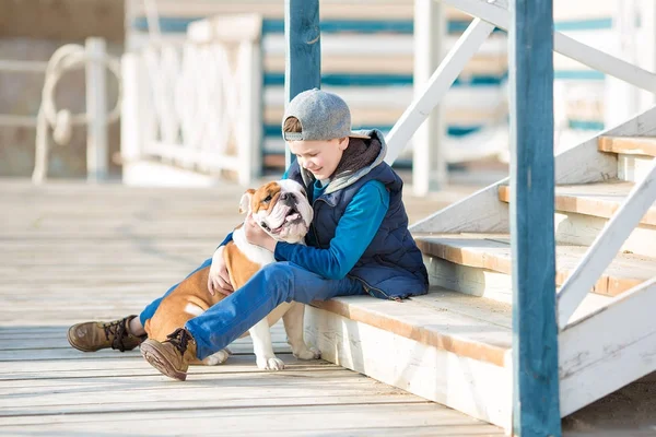Trevlig ser stilig pojke på stranden med bulldog — Stockfoto