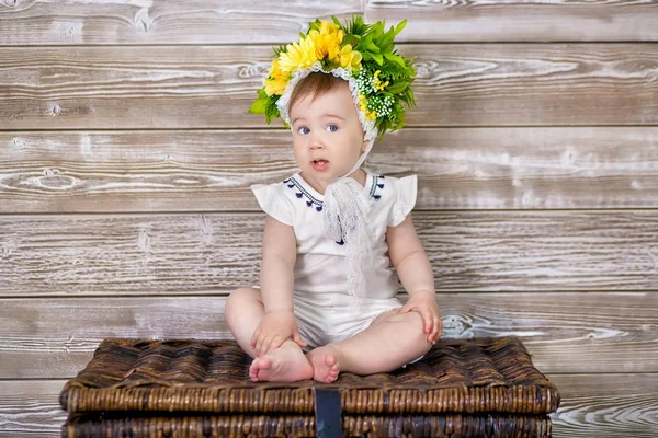 Portret cute dziewczynka na jasnym tle z wieniec z kwiatów na głowie siedzi na kanapie kosz — Zdjęcie stockowe