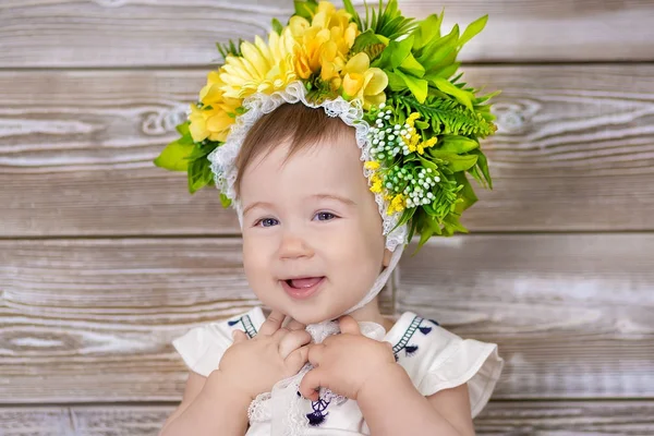 Retrato de um bebê bonito menina em um fundo leve com uma coroa de flores em sua cabeça sentado no sofá cesta — Fotografia de Stock