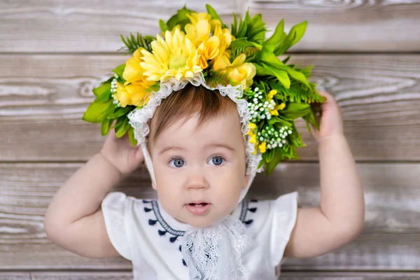 Portret cute dziewczynka na jasnym tle z wieniec z kwiatów na głowie siedzi na kanapie kosz — Zdjęcie stockowe