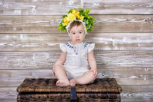 Porträtt av en söt flicka på en ljus bakgrund med en krans av blommor på huvudet sitter på soffa korg — Stockfoto