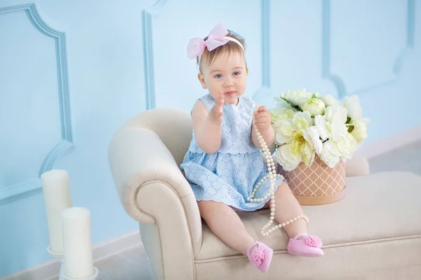 Portrait of a cute baby girl on a light background with a wreath of flowers on her head sitting on sofa basket — Stock Photo, Image