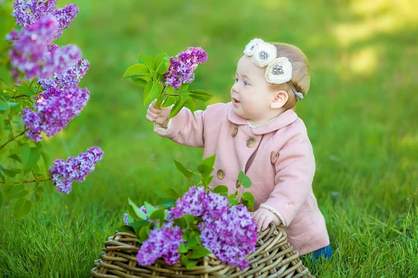 Смолящая девочка 1-2 лет в цветочном венке, держа букет лилака на улице. Смотрю в камеру. Летняя весна . — стоковое фото