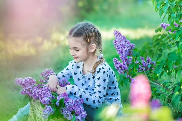 Улыбаясь маленькая милая блондинка девочка 4-9 лет с букетом сирени в руках в джинсах и рубашке — стоковое фото