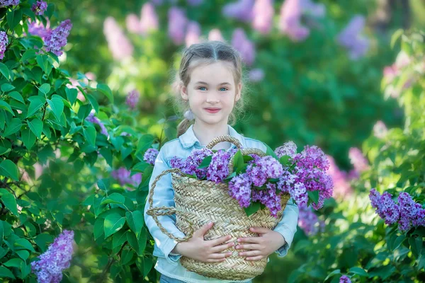 Улыбаясь маленькая милая блондинка девочка 4-9 лет с букетом сирени в руках в джинсах и рубашке — стоковое фото