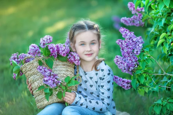 Sonriente niña rubia linda 4-9 años con un ramo de lila en las manos en jeans y camisa — Foto de Stock