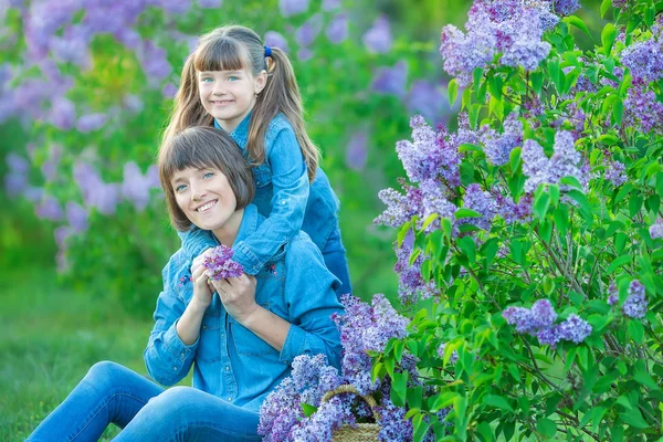 Aranyos és imádnivaló gyönyörű anya hölgy anya nő réten lila lila bokor barna lány lányával. Emberek farmert hord. — Stock Fotó