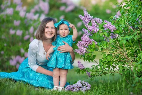 Happy mother mom with daughter enjoying time on a awesome place between lilac syringe bush.Young ladies with basket full of flowers dressed in jeans and stylish shirts relaxing in a cloud of scent.