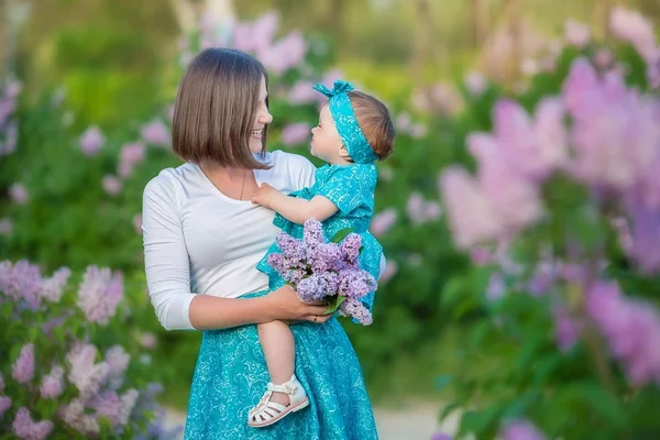 Mère heureuse maman avec sa fille profiter du temps sur un endroit génial entre lilas seringue bush.Young dames avec panier plein de fleurs vêtues de jeans et chemises élégantes se détendre dans un nuage de parfum . — Photo