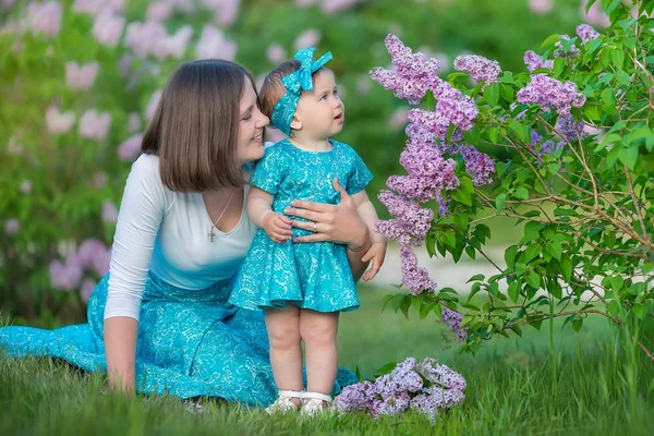 Boldog anya anya lánya élvezi idő egy fantasztikus helyen között bush lila fecskendő. Fiatal női kosár virágokkal teli öltözött farmert és elegáns ing pihentető egy felhő, illat. — Stock Fotó