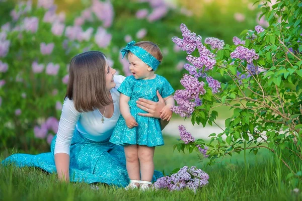 Boldog anya anya lánya élvezi idő egy fantasztikus helyen között bush lila fecskendő. Fiatal női kosár virágokkal teli öltözött farmert és elegáns ing pihentető egy felhő, illat. — Stock Fotó