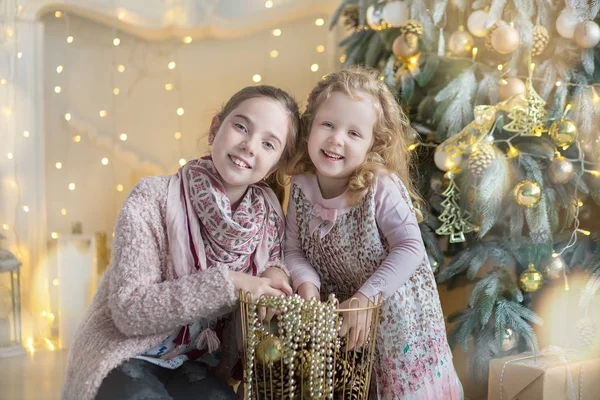 お菓子とスタイリッシュなドレスでおもちゃがいっぱいクリスマス ツリーの近くに新しい年のクリスマスを祝う 2 つのかわいい素晴らしい女の子姉妹 — ストック写真