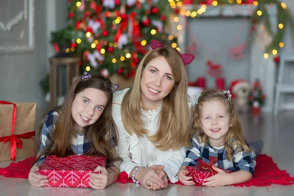 Söt awesome blond mor mamma med två flickor döttrar firar nyår jul nära xmas träd fullt av leksaker i eleganta klänningar med godis — Stockfoto