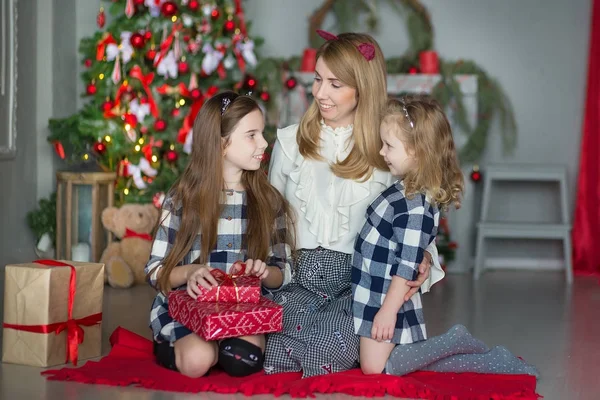 お菓子とスタイリッシュなドレスでおもちゃがいっぱいクリスマス ツリーの近くに新しい年のクリスマスを祝う二人の女の子の娘かわいい素晴らしい金髪母のママ — ストック写真