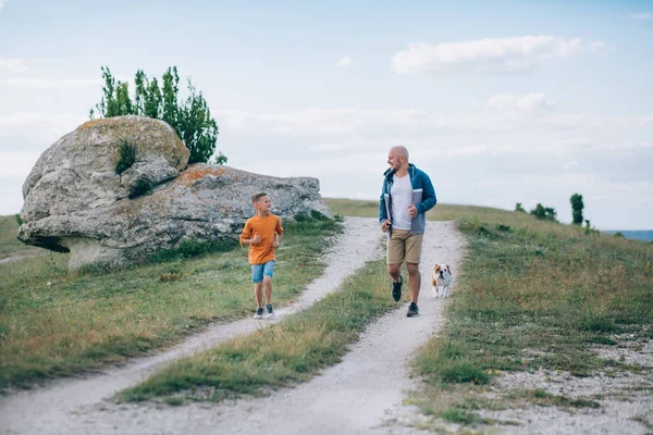 Papá e hijo corriendo en el campo con el perro — Foto de Stock