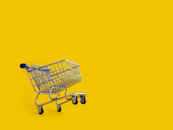 Leere Einkaufswagen vor gelbem Hintergrund — Stockfoto