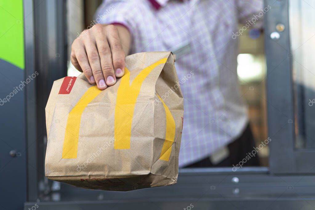 Sankt-Petersburg/Russia - July 21 2019: McDonalds worker holding cup with coca-cola. Hand with a paper cup with a straw through the window of mcdonalds car drive thru service.