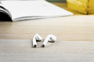 Modern beyaz kablosuz kulaklıklar arka planda açık kitaplarla ahşap masada.