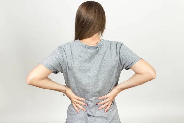 Hübsche Frau leidet unter Rückenschmerzen vor grauem Hintergrund — Stockfoto
