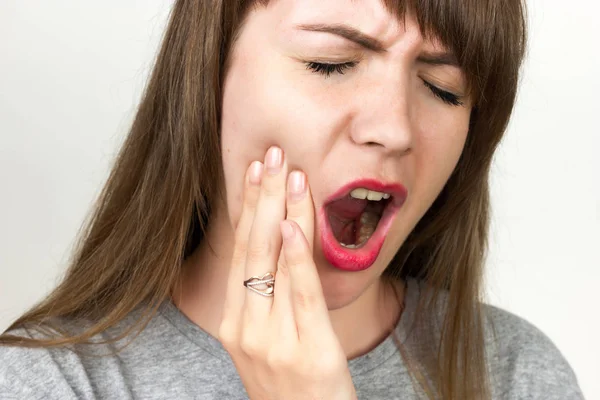 Ritratto ravvicinato di una bella donna che ha mal di denti in piedi su sfondo grigio — Foto Stock