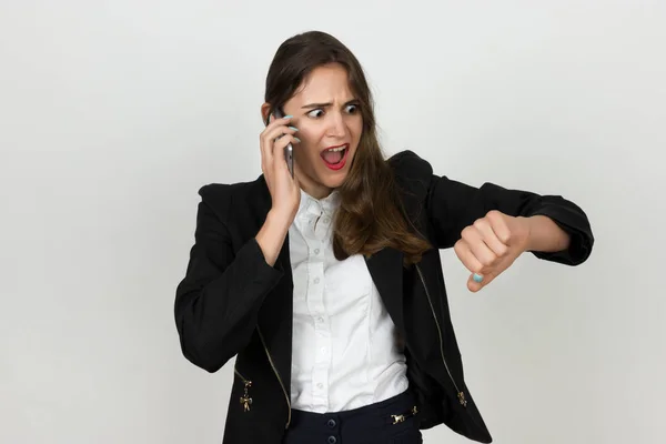 Retrato de una joven y bonita empresaria hablando por teléfono y mirando a la mano grita y muestra un gesto "Llegas tarde " —  Fotos de Stock