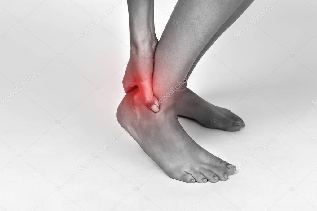Woman hand holding her beautiful healthy foot and massaging ankle in pain area. Black and white with red accent. Pain concept close-up