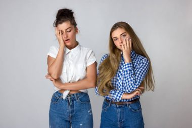 Gri bir arka plan üzerinde iki yorgun genç kız kardeş.