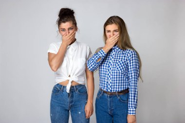 Kötü bir koku yüzünden burnunu tutarak gri arka plan üzerinde iki genç ve güzel kız portresi