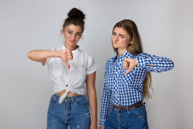 Başparmak aşağı gri arka plan üzerinde duran ve kameraya bakarak gösterilen iki genç kız portresi