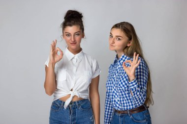 Gri arka plan üzerinde duran ve kameraya bakarak ok işaret gösteren bir iki genç kız portresi