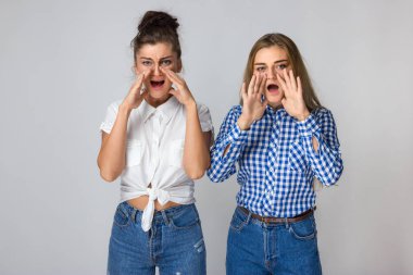 Çığlık atan iki genç kız portresi iki eli onu yüz ayakta gri arka plan üzerinde koymak