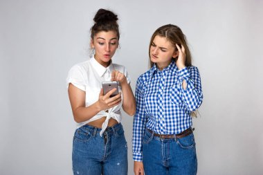 İki genç kız kardeş düşünüyor ve telefona gri arka plan üzerinde görünüyor portresi