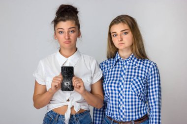 İki üzgün genç kız kardeş. Gri arka plan üzerinde Smartphone ile kırık ekran ayakta tutan genç kadın