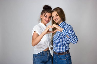 İki genç kız kardeşi gri arka plan üzerinde parmak ile kalp yapma.