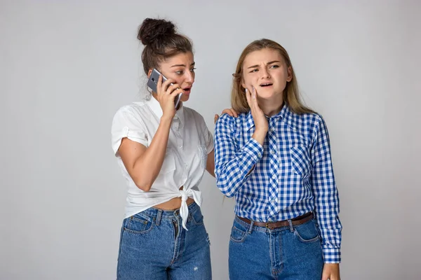 Diş ağrısı olan güzel bir kadın portresi kız kardeşi gri arka plan üzerinde duran bir doktor çağırır.