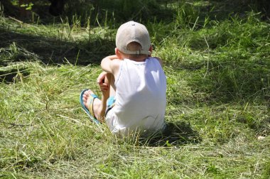 Rahatsız çocuk çimlerde oturuyor.