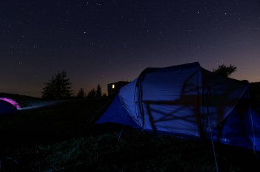 Dağın tepesinde çadır altında yıldızlı gece.