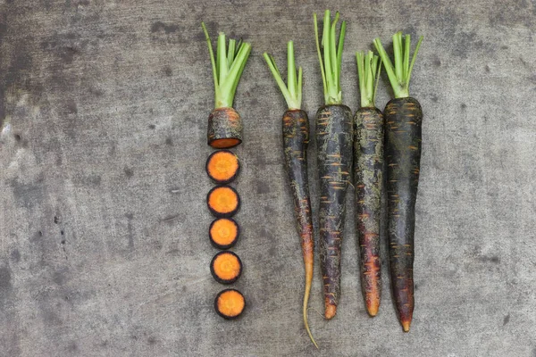 black carrots and some cut pieces on a grungy metal background