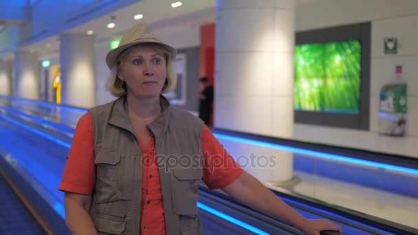 Uma turista mulher está de pé em uma escada rolante em movimento no aeroporto . — Vídeo de Stock